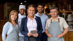 A business owner standing in the doorway with their employees. The owner worked with White Oak Insurance Services to get the right Business Insurance for her business. (The image is fictitious)